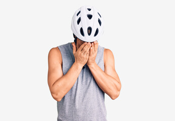 Young handsome man wearing bike helmet with sad expression covering face with hands while crying. depression concept.