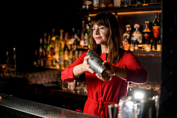 Fototapeta na wymiar view of young beautiful woman bartender stands behind bar with shaker in her hands