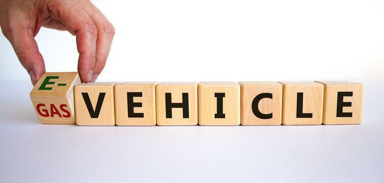 Gas vehicle or e-vehicle. Hand turns a cube and changes words 'gas vehicle' to 'e-vehicle'. Beautiful yelow table, white background, copy space. Business and electric vehicle concept.