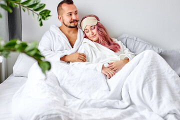 couple spend time on bed in the morning, adorable married man and woman in bathrobes at weekends, have rest. love concept