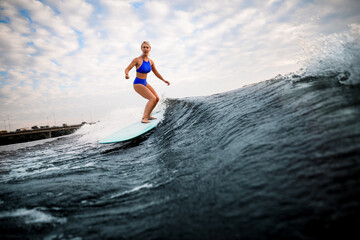 blonde woman in blue swimsuit rides down the wave on surfboard.