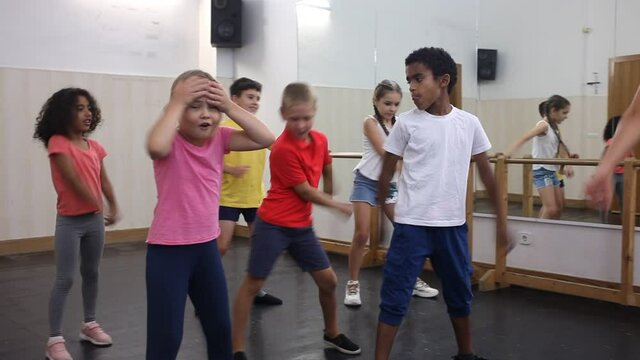 Preteen boys and girls with female trainer practicing floss dance movements, swinging hips and arms during group class. High quality FullHD footage