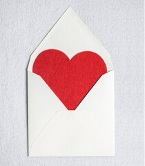 Top view of an open envelope with red felt heart on a white felt background. The concept of Valentine's Day