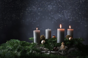 Third advent with three burning candles on fir branches with Christmas decoration against a dark...