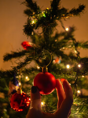 Hand of female decorating christmas tree with red ball