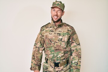 Young caucasian man wearing camouflage army uniform winking looking at the camera with sexy...