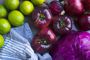 Fresh fruits and vegetables. Organic limes, red onions, red cabbage, purple tomatoes. Dark heirloom tomatoes. Farmer's market winter harvest.