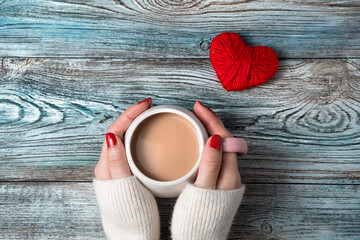 Hands of a woman holding a Cup of coffee with milk on a romantic background. Top view, with space to copy. Concept February 14.
