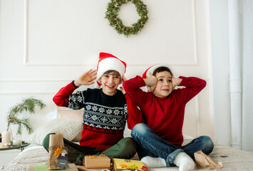 Fototapeta premium Cute boys brothers pack Christmas gifts sitting on the bed at home. new year surprise