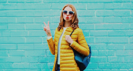 Portrait of young woman wearing a yellow jacket over a blue brick wall background