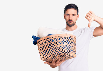 Young handsome man holding laundry basket with angry face, negative sign showing dislike with...