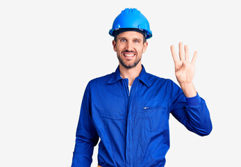 Young handsome man wearing worker uniform and hardhat showing and pointing up with fingers number four while smiling confident and happy.