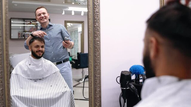 Young man in barber shop sits in an armchair. Barber cuts his hair with a trimer