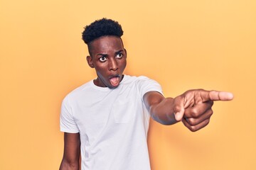 Young african american man wearing casual clothes pointing with finger surprised ahead, open mouth amazed expression, something on the front