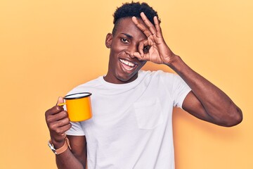 Young african american man holding coffee smiling happy doing ok sign with hand on eye looking through fingers