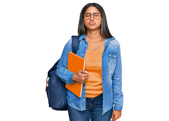 Young latin girl wearing student backpack and holding books looking at the camera blowing a kiss on air being lovely and sexy. love expression.