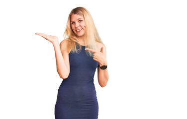 Fototapeta premium Young beautiful blonde woman wearing casual dress amazed and smiling to the camera while presenting with hand and pointing with finger.