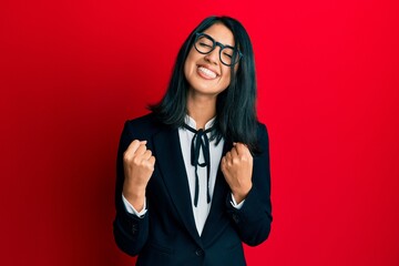 Beautiful asian young woman wearing business suit very happy and excited doing winner gesture with arms raised, smiling and screaming for success. celebration concept.
