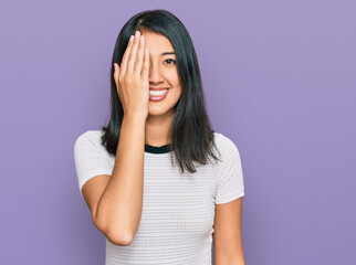 Beautiful asian young woman wearing casual white t shirt covering one eye with hand, confident smile on face and surprise emotion.