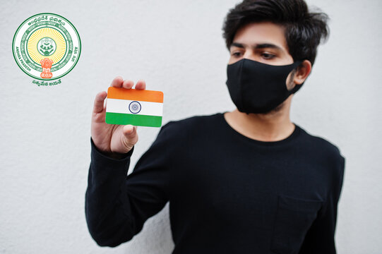 Indian man wear all black and face mask, hold India flag in hand isolated on white background with Andhra Pradesh state emblem . Coronavirus India states and union territories concept.