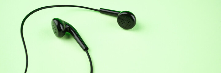 black earphones over green background with copy space. above view. stereo music symbol. banner template