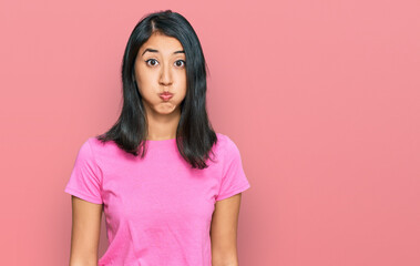 Fototapeta premium Beautiful asian young woman wearing casual pink t shirt puffing cheeks with funny face. mouth inflated with air, crazy expression.