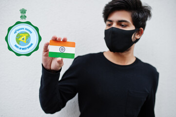 Indian man wear all black and face mask, hold India flag in hand isolated on white background with West Bengal state emblem . Coronavirus India states and union territories concept.