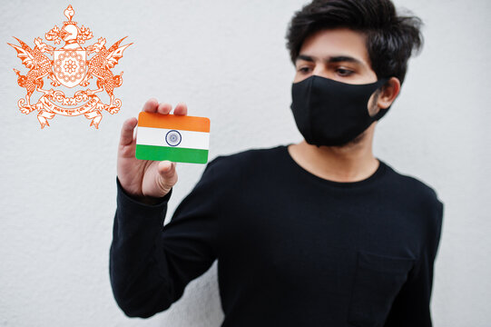 Indian man wear all black and face mask, hold India flag in hand isolated on white background with Sikkim state emblem . Coronavirus India states and union territories concept.