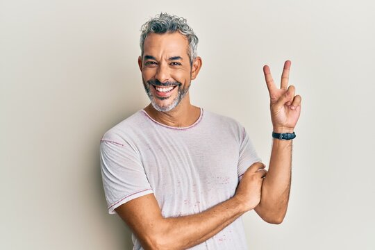 Middle age grey-haired man wearing casual clothes smiling with happy face winking at the camera doing victory sign. number two.
