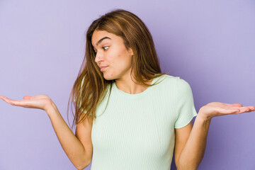Young skinny caucasian girl teenager on purple background confused and doubtful shrugging shoulders to hold a copy space.