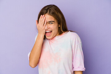 Young skinny caucasian girl teenager on purple background having fun covering half of face with palm.