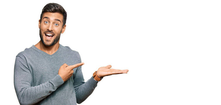 Handsome hispanic man wearing casual clothes amazed and smiling to the camera while presenting with hand and pointing with finger.