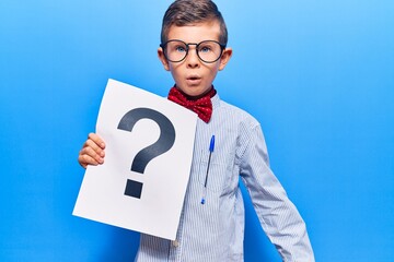 Cute blond kid wearing nerd bow tie and glasses holding question mark scared and amazed with open...