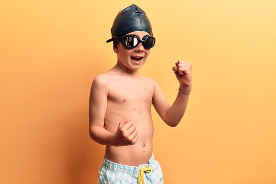 Cute blond kid wearing swimwear and swimmer glasses celebrating surprised and amazed for success with arms raised and eyes closed