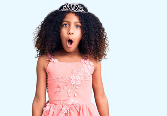 African american child with curly hair wearing princess crown scared and amazed with open mouth for...