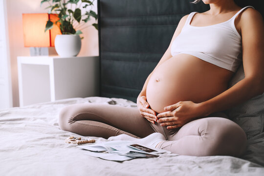 Pregnant woman holds hands on her belly at home interior