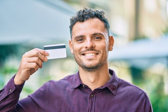 Young hispanic man smiling happy holding credit card at the city.