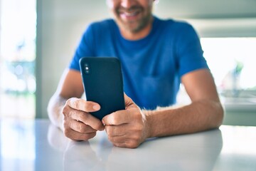 Young irish man smiling happy using smartphone sitting on the table at home.