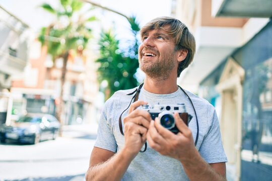 Young irish photographer man smiling happy using vintage camera at street of city.