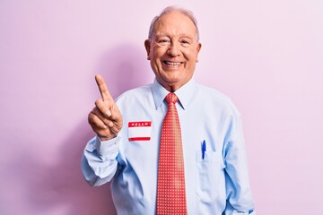 Senior handsome grey-haired businessman wearing tie and shirt with name presentation sticker smiling with an idea or question pointing finger up with happy face, number one