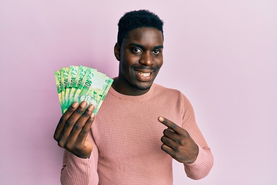 Handsome black man holding south african 10 rand banknotes smiling happy pointing with hand and finger