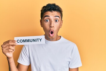 Young handsome african american man holding community baner as social cooperation scared and amazed with open mouth for surprise, disbelief face