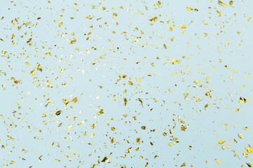 Gold confetti on light blue paper background. Festive holiday backdrop. Birthday congratulations...