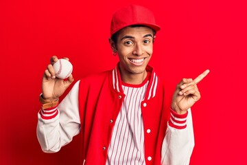 Young african amercian man wearing baseball uniform holding ball smiling happy pointing with hand and finger to the side