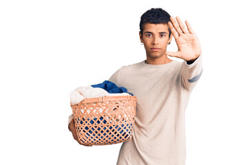 Young african amercian man holding laundry basket with open hand doing stop sign with serious and confident expression, defense gesture