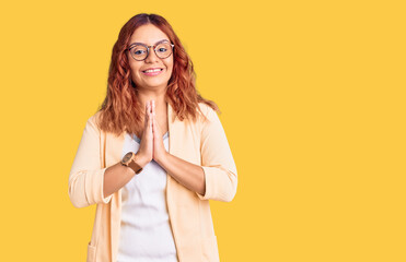 Young latin woman wearing business clothes praying with hands together asking for forgiveness smiling confident.