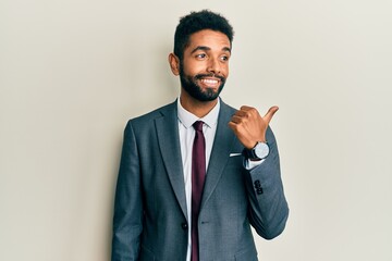 Handsome hispanic man with beard wearing business suit and tie smiling with happy face looking and pointing to the side with thumb up.
