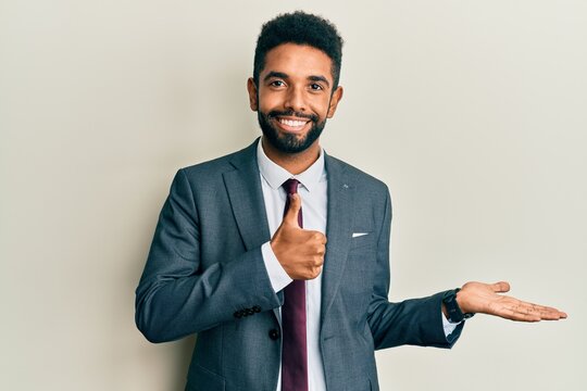 Handsome hispanic man with beard wearing business suit and tie showing palm hand and doing ok gesture with thumbs up, smiling happy and cheerful