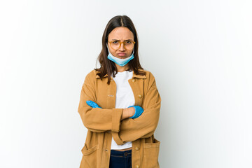 Fototapeta na wymiar Young latin woman wearing a mask to protect from covid isolated on white background frowning face in displeasure, keeps arms folded.