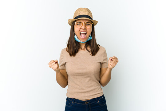 Young latin woman wearing hat and mask to protect from covid isolated on white background cheering carefree and excited. Victory concept.